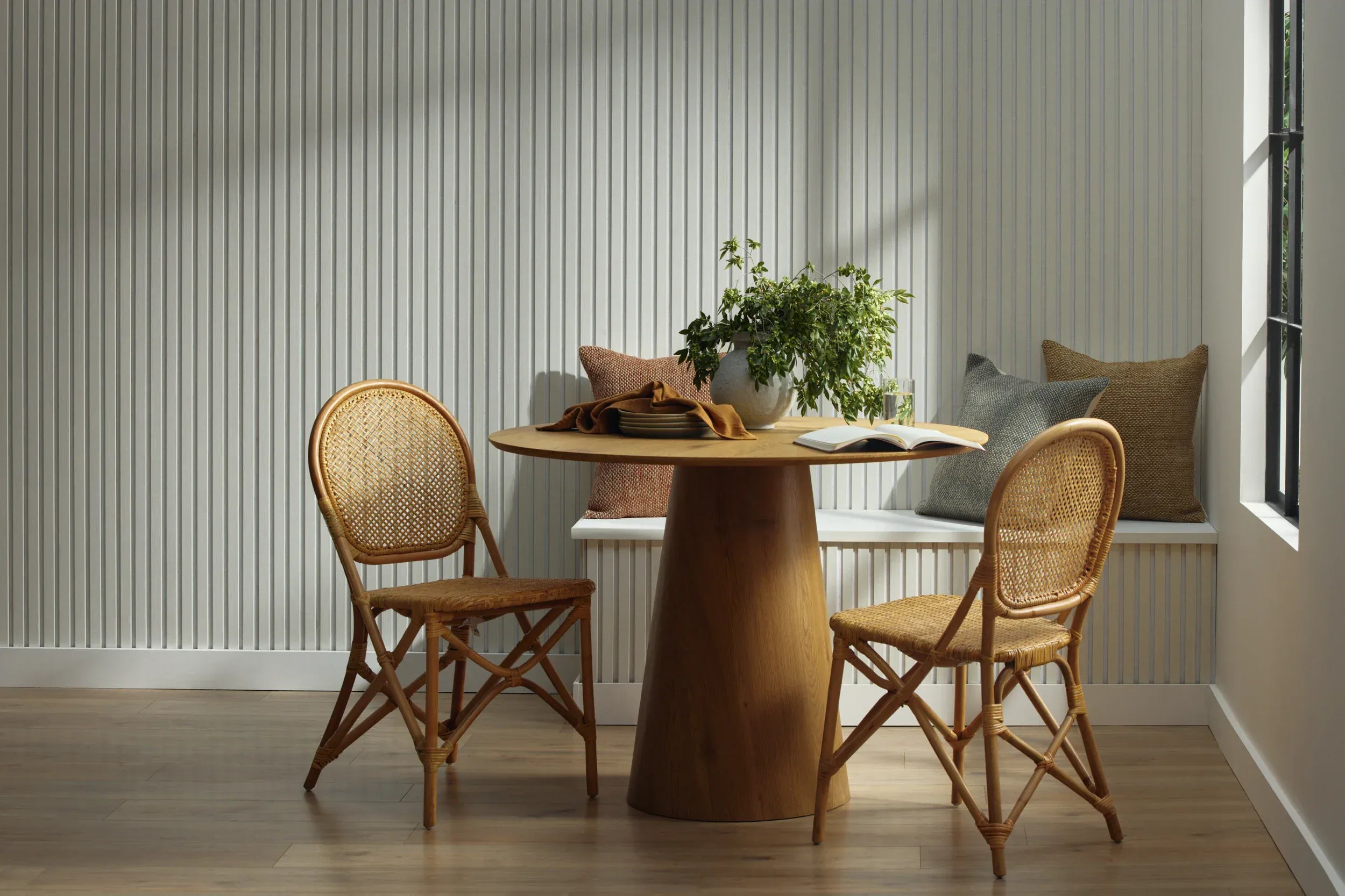 Wooden dining table with two chairs in a room with a white wood wall panel feature wall and window.